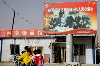 In this Sept. 20, 2018, file photo, an Uyghur woman uses an electric-powered scooter to fetch school children as they ride past a picture showing China's President Xi Jinping joining hands with a group of Uighur elders.