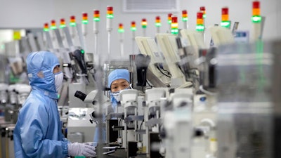 In this May 14, 2020, file photo, employees wearing protective equipment work at a semiconductor production facility for Renesas Electronics during a government organized tour for journalists in Beijing. China has announced tax breaks to spur growth of its semiconductor industry following U.S. sanctions that cut off access to American processor chips for tech giant Huawei and some other companies.
