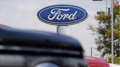In this file photo, the Ford logo hangs over a row of 2020 F-150 pickup trucks at a dealership in Denver.