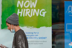 A man walks past a 'Now Hiring' sign on a window at Sherwin Williams store, Friday, Feb. 26, 2021, in Woodmere Village, Ohio. Massive fraud in the nation's unemployment system is raising alarms even as President Joe Biden and Congress prepare to pour hundreds of billions more into expanded benefits for those left jobless by the coronavirus pandemic.