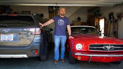 Steve Bock stands between his new Subaru Outback and his 1965 Ford Mustang at his home in Apex, N.C., on Friday, March 5, 2021. He would like to have an electric car, but says the prices will have to come down a lot before he can do it. Opinion polls show that most Americans would consider an EV if it cost less, if more charging stations existed and if a wider variety of models were available.