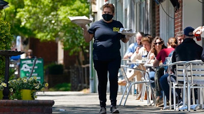 A member of the wait staff delivers food to outdoor diners along the sidewalk at the Mediterranean Deli restaurant in Chapel Hill, NC on April 16.