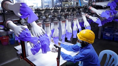 In this Aug. 26, 2020 photo, a worker inspects disposable gloves at the Top Glove factory in Shah Alam on the outskirts of Kuala Lumpur, Malaysia.