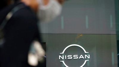 A man wearing a face mask to to help curb the spread of the coronavirus walks by the logo of Nissan seen at the automaker's showroom in Tokyo Tuesday, May 11, 2021. Nissan reduced its losses for January-March, compared to last year, as restructuring efforts kicked in, despite the sales damage from the coronavirus pandemic, the Japanese automaker said Tuesday.