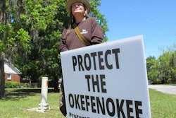 Jane Winkler stands with a sign outside a church where Georgia Gov. Brian Kemp met with local Chamber of Commerce members, Folkston, Ga., April 22, 2021.
