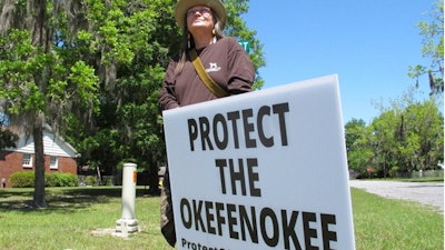 Jane Winkler stands with a sign outside a church where Georgia Gov. Brian Kemp met with local Chamber of Commerce members, Folkston, Ga., April 22, 2021.