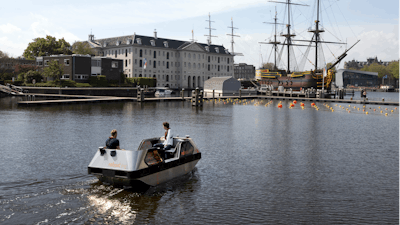 An electric boat steers close to a full-size replica of the 18th century three-mast trading ship Amsterdam at the National Maritime Museum, in Amsterdam, Thursday, May 20, 2021. Already steeped in maritime history, the city's more than 100 kilometers (60 miles) of waterways are to start hosting prototypes of futuristic boats — small, fully-autonomous electric vessels — to carry out tasks including transporting passengers and picking up garbage.