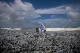 A Sri Lankan navy soldier clad in a protective suit walks on the mounds of debris that washed ashore from the burning Singaporean ship MV X-Press Pearl which is anchored off Colombo port at Kapungoda, out skirts of Colombo, Sri Lanka, Thursday, May 27, 2021.