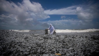 A Sri Lankan navy soldier clad in a protective suit walks on the mounds of debris that washed ashore from the burning Singaporean ship MV X-Press Pearl which is anchored off Colombo port at Kapungoda, out skirts of Colombo, Sri Lanka, Thursday, May 27, 2021.