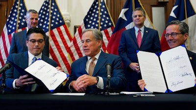 With the help of state Rep. Chris Paddie, left, and state Sen. Kelly Hancock, right, Texas Gov. Greg Abbott, center, displays two energy related bills he signed, Tuesday, June 8, 2021, in Austin, Texas. Abbot signed legislation into law to reform the Electric Reliability Council of Texas (ERCOT) and weatherize and improve the reliability of the state's power grid.