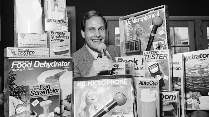 In this Wednesday, Dec. 8, 1982 file photo, Ron Popeil, the man behind those late-night, rapid-fire television commercials that sell everything from the Mr. Microphone to the Pocket Fisherman to the classic Veg-a-Matic, sits surrounded by his wares in his office in Beverly Hills, Calif. Ron Popeil, the quintessential TV pitchman and inventor known to generations of viewers for hawking products including the Veg-O-Matic, the Chop-O-Matic, Mr. Microphone and the Showtime Rotisserie and BBQ, died Wednesday, July 28, 2021 his family said.