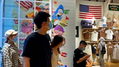 People wearing face masks visit a fashion boutique displaying an American flag in Beijing, Sunday, July 11, 2021. China on Sunday said it will take 'necessary measures' to respond to the U.S. blacklisting of Chinese companies over their alleged role in abuses of Uyghur people and other Muslim ethnic minorities.