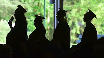 In this Friday, June 1, 2018,, file photo, graduates are silhouetted against the green landscape as they line up to receive their diplomas at Berkshire Community College's commencement exercises at the Shed at Tanglewood in Lenox, Mass. Critics of traditional four-year degree programs say grads leave burdened with student loans and no clear path to a career. But experts say the four-year degree is still a good investment since it leads to higher overall lifetime earnings compared to workers without a degree.