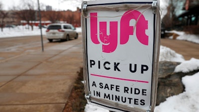 In this Wednesday, Feb. 12, 2020, photo, a sign marks the pick lane for Lyft car share service outside the Pepsi Center in downtown Denver. Ford Motor Co. and a self-driving vehicle company it partly owns will join with the Lyft ride-hailing service to offer autonomous rides on the Lyft network. The service using Ford vehicles and a driving system developed by Argo AI will begin in Miami later this year and start in Austin, Texas, in 2022.