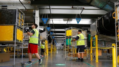 In this Dec. 17, 2019, file photo, Amazon workers move containers to delivery trucks at an Amazon warehouse facility in Goodyear, Ariz. Starting Monday, Aug. 9, 2021, Amazon will be requiring all of its 900,000 U.S. warehouse workers to wear masks indoors, regardless of their vaccination status. The move follows steps by a slew of other retailers, including Walmart and Target, to mandate masks for their workers. In many of those cases the mandates apply to workers in locations of substantial COVID-19 transmission.