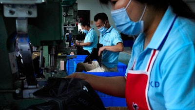 In this July 15, 2021, file photo, workers wearing face masks to help curb the spread of the coronavirus assembly ice-skating shoes at a manufacturing factory in the ice and snow sports equipment industry park in Zhangjiakou in northwestern China's Hebei province. China’s factory activity decelerated in August as export demand weakened, a survey showed Tuesday, Aug. 31, 2021. The monthly purchasing managers’ index of the Chinese statistics bureau and an official industry group declined to 50.1 from July’s 50.4 on a 100-point scale on which numbers above 50 show activity increasing.