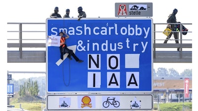 An activist hangs from a gantry over the A9 motorway near Fürholzen in the direction of Munich during a banner campaign, holding a banner with the words 'Destroy cars' in his hands while police officers from a special task force get into position on the gantry, Tuesday, Sept.7, 2021. The activists have pasted over the traffic sign with the words 'smashcarlobby & industry - NO IAA.'