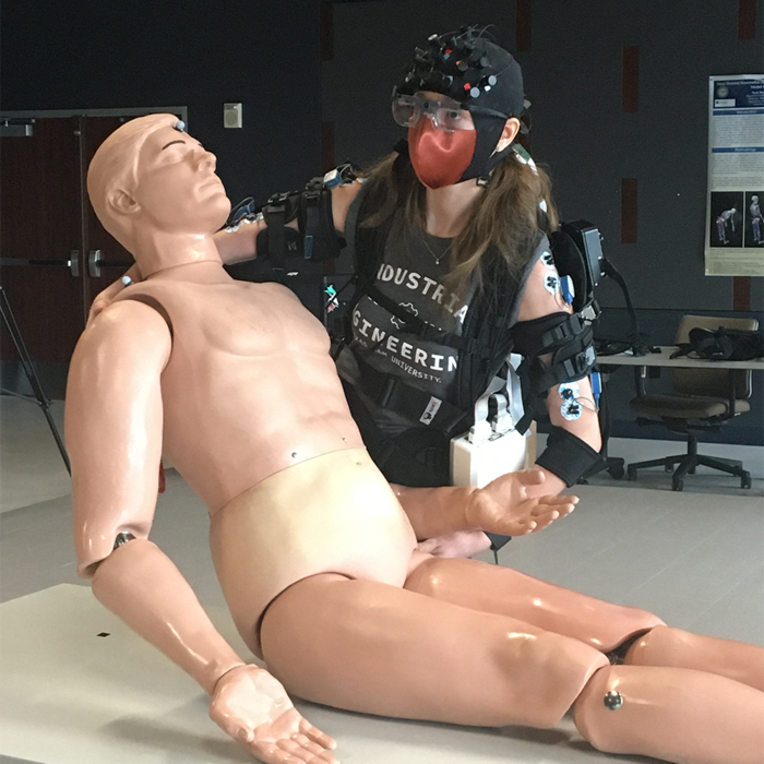 Doctoral student Sarah Hopko is wearing an exoskeleton while performing patient handling tasks. Her brain activity is being tracked using Near Infrared Spectroscopy, gaze behavior is being tracked using eye tracking and muscle activity through electromyographic sensors.