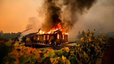 Vines surround a burning building as the Kincade Fire burns through the Jimtown community of unincorporated Sonoma County, Calif., on Oct. 24, 2019. Pacific Gas & Electric has reached a settlement agreement, Nov. 3, 2021, with state regulators over the 2019 Kincade fire, which was ignited by the utility's electrical transmission equipment in a remote area of Sonoma County.