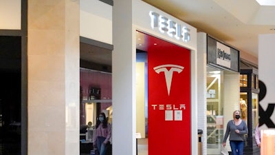 This photo made Wednesday, Feb. 24, 2021, shows people walking by the entrance to a Tesla store at a shopping mall in Pittsburgh. Tesla shares slumped about 5% in premarket trading after its CEO Elon Musk said he would sell 10% of his holdings — about $20 billion worth — in the electric car maker based on the results of a poll he conducted on Twitter over the weekend.