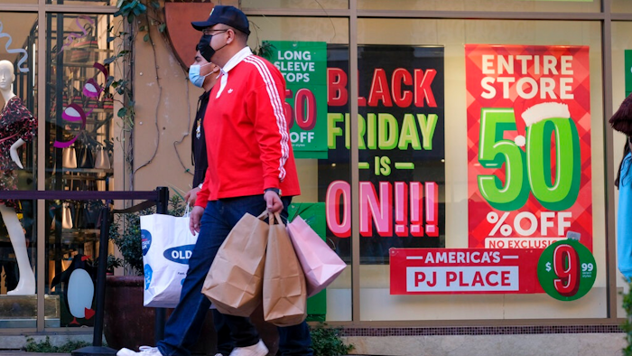Black Friday shoppers, wearing face masks, carry bags at the Citadel Outlets in Commerce, Calif., Friday, Nov. 26, 2021. Americans slowed their spending in November from October but they showed another month of resilience against higher prices and shortages in stores.