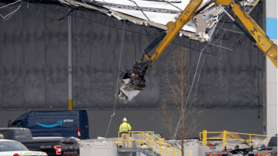 Workers use equipment to remove a section of roof left on a heavily damaged Amazon fulfillment center on Dec. 11, 2021 in Edwardsville, IL.