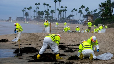 Workers in protective suits clean the contaminated beach in Corona Del Mar after an oil spill off the Southern California coast, on Oct. 7, 2021. A Los Angeles federal grand jury on Wednesday, Dec. 15 charged a Houston-based oil company and two subsidiaries for the oil spill off the California coast in October.