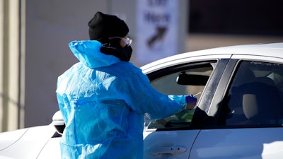A medical technician performs a nasal swab test on a motorist queued up in a line at a COVID-19 testing site near All City Stadium Dec. 30, 2021, in southeast Denver. Millions of workers whose jobs don’t provide paid sick days are having to choose between their health and their paycheck as the omicron variant of COVID-19 rages across the nation. While many companies instituted more robust sick leave policies at the beginning of the pandemic, those have since been scaled back with the rollout of the vaccines, even though the omicron variant has managed to evade them.
