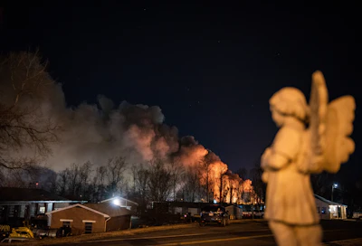 An angel statue faces in the direction of billowing smoke from a fire at the Weaver Fertilizer Plant on Monday, Jan. 31, 2022, in Winston-Salem, N.C.