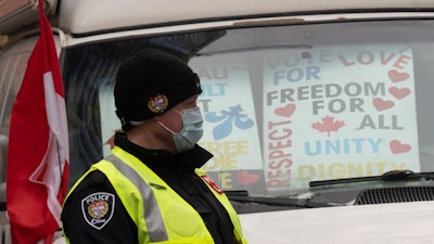 A police officer walks among protest vehicles as he distributes notices to protesters, Wednesday, Feb. 16, 2022 in Ottawa.