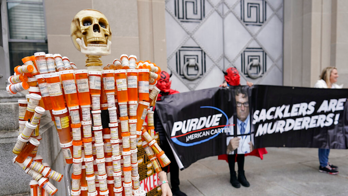 Pill Mann' made by Frank Huntley of Worcester, Mass., from his opioid prescription pill bottles, is displayed during a protest by advocates for opioid victims outside the Department of Justice, on Dec. 3, 2021, in Washington. Many families left heartbroken by opioid overdoses and addictions have been waiting for years to be able to tell another family – the Sacklers – about the damage their company, Purdue Pharma, did. Their chance arrives Thursday, March 10, 2022, in a federal court hearing to be conducted by video, during what could be the end of a long legal odyssey that will allow Purdue and the Sacklers to settle thousands of lawsuits.