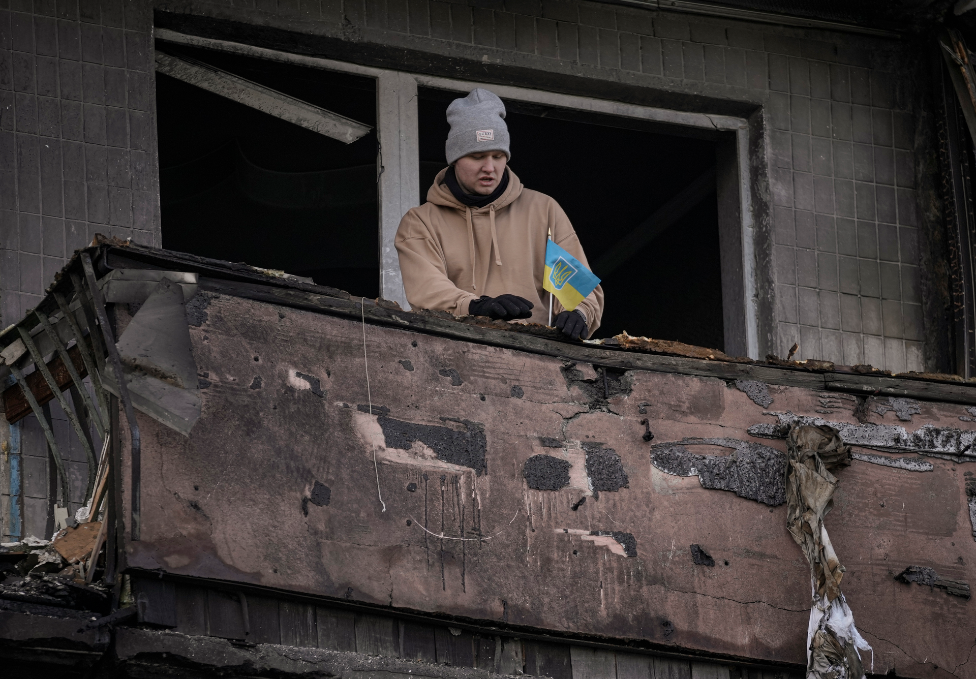 A man places a small Ukrainian flag on a burnt balcony of an apartment hit by an artillery strike, Kyiv, March 14, 2022.