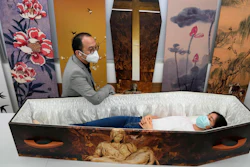 Wilson Tong, CEO of LifeArt Asia, left, talks to a reporter who tries out a catholic-designed paper coffin at Tong's factory in Hong Kong, March 18, 2022.
