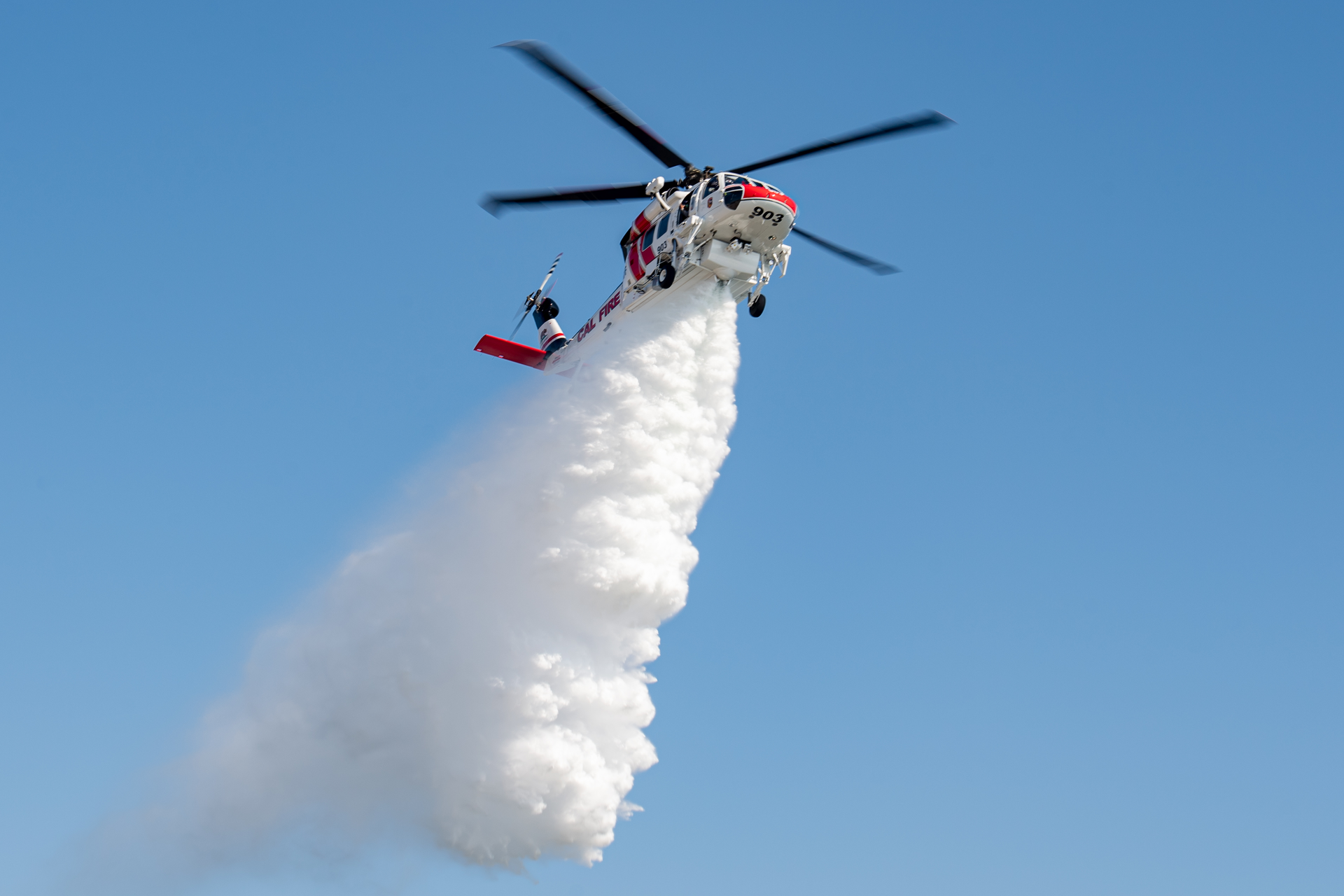 A Firehawk aircraft operated by CAL FIRE demonstrates the powerful concentration of water released from its 1,000 gallon tank for effective wildfire fighting.