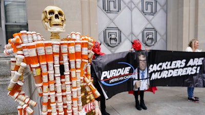 Pill Mann' made by Frank Huntley of Worcester, Mass., from his opioid prescription pill bottles, is displayed during a protest by advocates for opioid victims outside the Department of Justice, on Dec. 3, 2021, in Washington. Many families left heartbroken by opioid overdoses and addictions have been waiting for years to be able to tell another family – the Sacklers – about the damage their company, Purdue Pharma, did. Their chance arrives Thursday, March 10, 2022, in a federal court hearing to be conducted by video, during what could be the end of a long legal odyssey that will allow Purdue and the Sacklers to settle thousands of lawsuits.