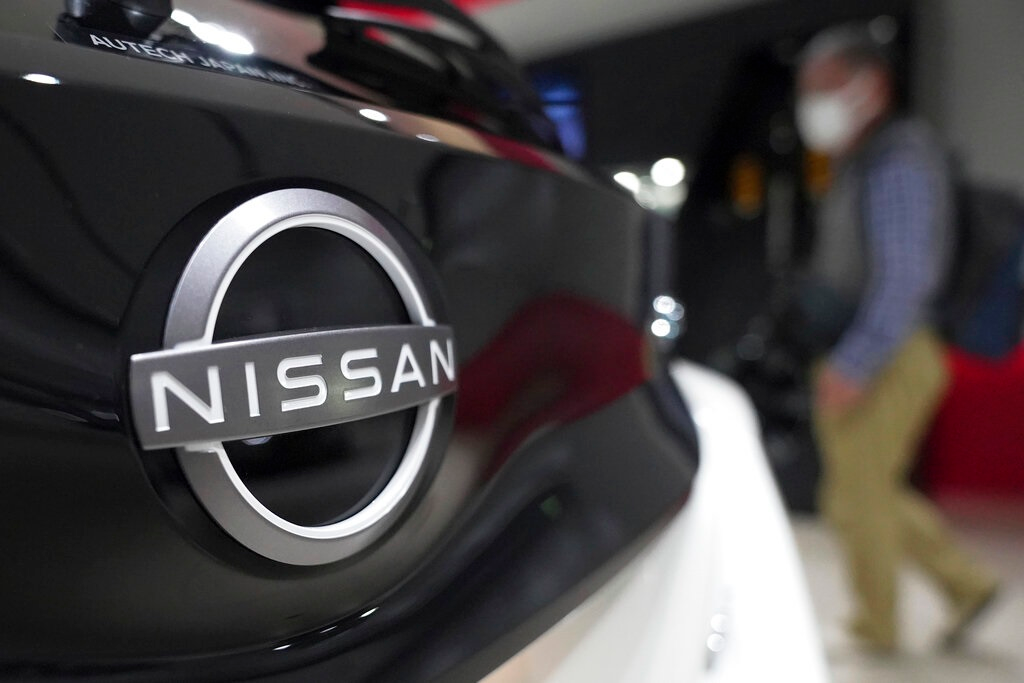 A visitor walks near a Nissan logo attached to a car at Nissan headquarters Thursday, May 12, 2022, in Yokohama near Tokyo. Japanese automaker Nissan returned to profitability in the last fiscal year for the first time in three years, despite challenges such as supply shortages caused by the pandemic and soaring costs.