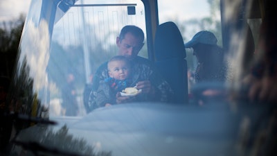 A man feeds a child as they arrive by bus at a reception center for displaced people in Zaporizhzhia, Ukraine, Monday, May 2, 2022. Thousands of Ukrainian continue to leave Russian occupied areas.