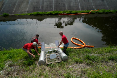 An employee of Osprey Initiative lays boom as the company installs a trap called a Litter Gitter to help collect trash floating in a canal before it can travel into larger bodies of water in Metairie, La., Thursday, May 19, 2022. Many novel devices are being used or tested worldwide to trap plastic trash in rivers and smaller streams before it can get into the ocean.