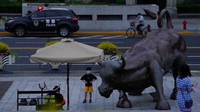 A child poses for a photo near a sculpture of a bull along the bund as day breaks, Wednesday, June 1, 2022, in Shanghai. Shanghai authorities say they will take major steps Wednesday toward reopening China's largest city after a two-month COVID-19 lockdown that has set back the national economy and largely confined millions of people to their homes.