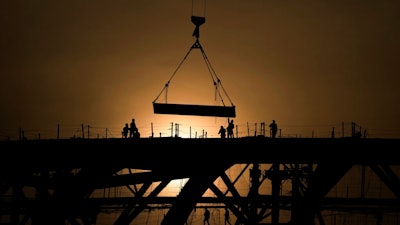 Workers are silhouetted against a sunset as they handle a steel frame on the roof of the Workers' Stadium under construction in Beijing, China, Monday, Feb. 28, 2022. China, the world’s top emitter of carbon dioxide and other greenhouse gases that cause global warming, has seen a notable dip in its carbon emissions over the past three quarters, as of June 1, 2022 — but it’s not clear how long the drop will continue.