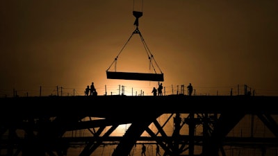 Workers are silhouetted against a sunset as they handle a steel frame on the roof of the Workers' Stadium under construction in Beijing, China, Monday, Feb. 28, 2022. China, the world’s top emitter of carbon dioxide and other greenhouse gases that cause global warming, has seen a notable dip in its carbon emissions over the past three quarters, as of June 1, 2022 — but it’s not clear how long the drop will continue.
