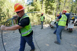Carl Roath, left, a worker with the Mason County (Wash.) Public Utility District, pulls fiber optic cable off of a spool, as he works with a team to install broadband internet service to homes in a rural area surrounding Lake Christine near Belfair, Wash., on Aug. 4, 2021. Federal officials announced plans Thursday, July 28, 2022, to spend $401 million in grants and loans to expand the reach and improve the speed of internet for rural residents, tribes and businesses in 11 West and Central U.S. states.