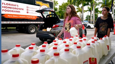 Vanessa Correa, left, and Gigi Fiske, right, pass out gallons of milk at a food distribution held by the Farm Share food bank, Wednesday, July 20, 2022, in Miami. Long lines are back at food banks around the U.S. as working Americans overwhelmed by inflation turn to handouts to help feed their families.