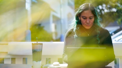 Daniella Malave works on her laptop at a coffee shop in Sea Girt, N.J., Thursday, Sept. 29, 2022. While working full time for Chipotle, Malave completed two years of community college with annual stipends of $5,250 from the restaurant chain. After that, she enrolled in the company’s free online college program, through which she earned a bachelor’s degree in business management from Wilmington University in 2020.