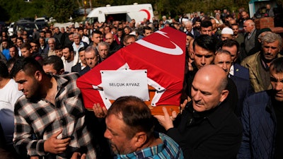 Turkey's Interior Minister Suleyman Soylu, right, helps a coffin covered with a Turkish flag of one of the miners killed in a coal mine explosion, during his funeral in Amasra, in the Black Sea coastal province of Bartin, Turkey, Saturday, Oct. 15, 2022. An official says an explosion inside a coal mine in northern Turkey has trapped dozens of miners. At least 14 have come out alive. The cause of Friday's blast in the town of Amasra in the Black Sea coastal province of Bartin was not immediately known.