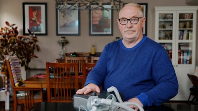 Jeffrey Reed, who experienced persistent sinus infections and two bouts of pneumonia while using a Philips CPAP machine, poses with the device at his home Thursday, Oct. 20, 2022, in Marysville, Ohio.