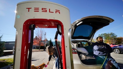 Janet Sanidad and her husband, Marc Sanidad, of Chantilly, Va., take a break to feed their dog while charging their Tesla, Wednesday, Oct. 19, 2022, in Freeport, Maine.