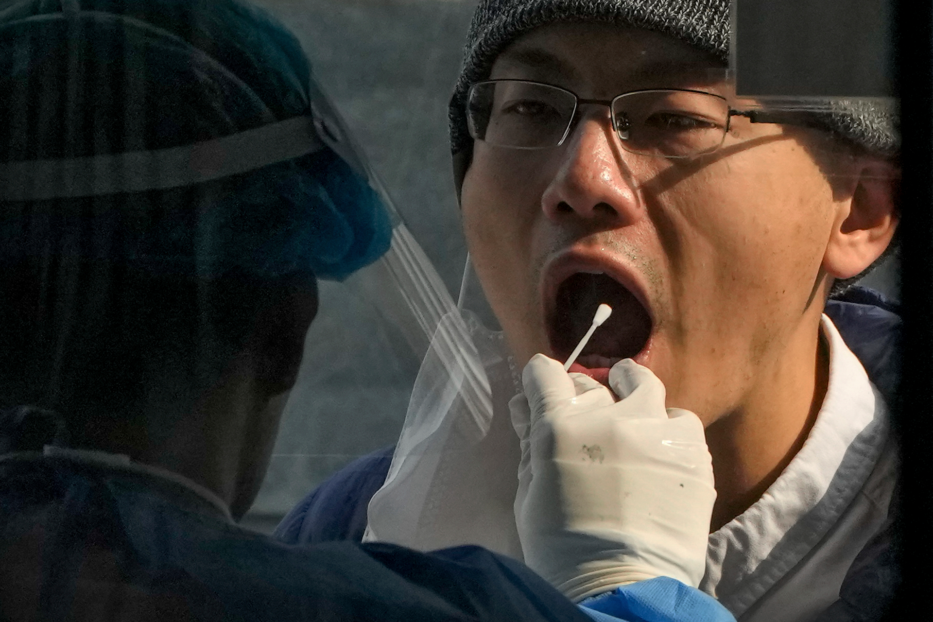 A medical worker collects a sample from a man at a coronavirus testing site in Beijing, Wednesday, Nov. 2, 2022.