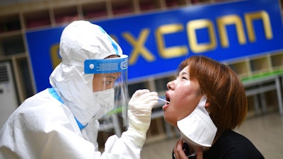 A medical worker takes a swab sample to test for COVID-19 from a worker at the Foxconn factory in Wuhan in central China's Hubei province Thursday, Aug. 5, 2021. Foxconn, the company that assembles Apple Inc.’s iPhones, has announced it is easing COVID-19 restrictions at its largest factory, in Zhengzhou, central China, that led thousands of workers to quit and drastically slowed production.