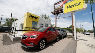 This May 23, 2020, photo shows rental vehicles parked outside a closed Hertz car rental office in south Denver.